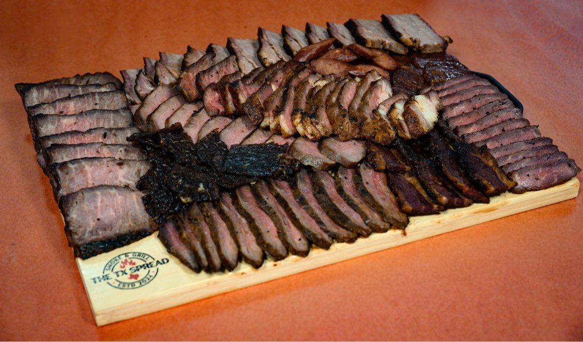 Tx Spread board at an angle with sliced smoked meats and a seared steak