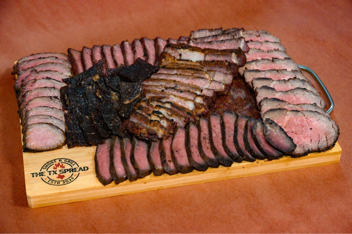 A Tx Spread board photographed at an angle, loaded with sliced smoked meats
