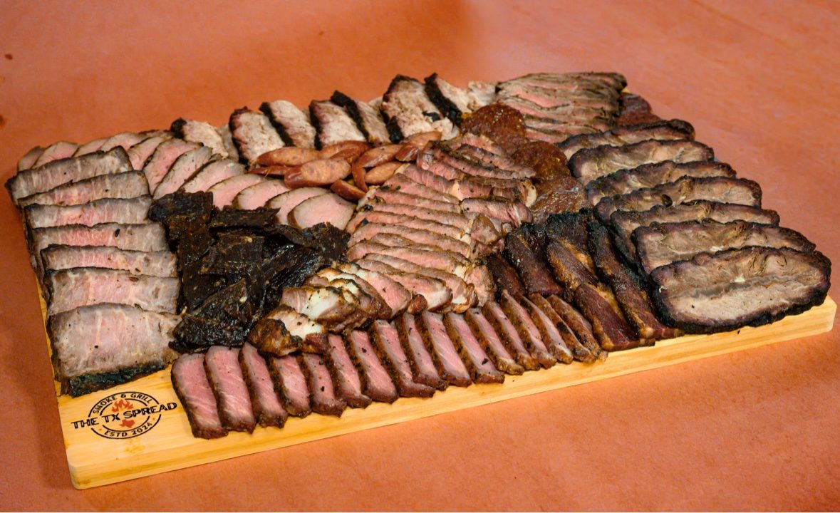 A wide Tx Spread board of sliced smoked meats photographed at an angle